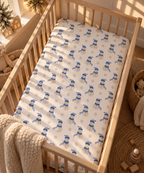 Blue Snowman Crib Sheet fitted in a wooden crib with a knit blanket over the rail