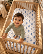 Toddler standing in a crib fitted with the Blue Snowman Crib Sheet