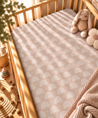 Blush Boho Rainbow Crib Sheet fitted in a wooden crib with a plush toy