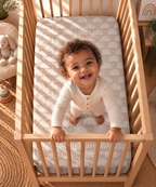 Toddler standing in a crib fitted with the Blush Boho Rainbow Crib Sheet