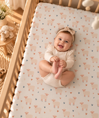 Smiling baby lying on the Cream Sheep Heart Crib Sheet