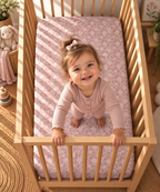 Toddler standing in a crib fitted with the Dusty Rose Lace Floral Crib Sheet