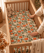 Hands smoothing the Green Gingham Pumpkin Crib Sheet over a crib mattress