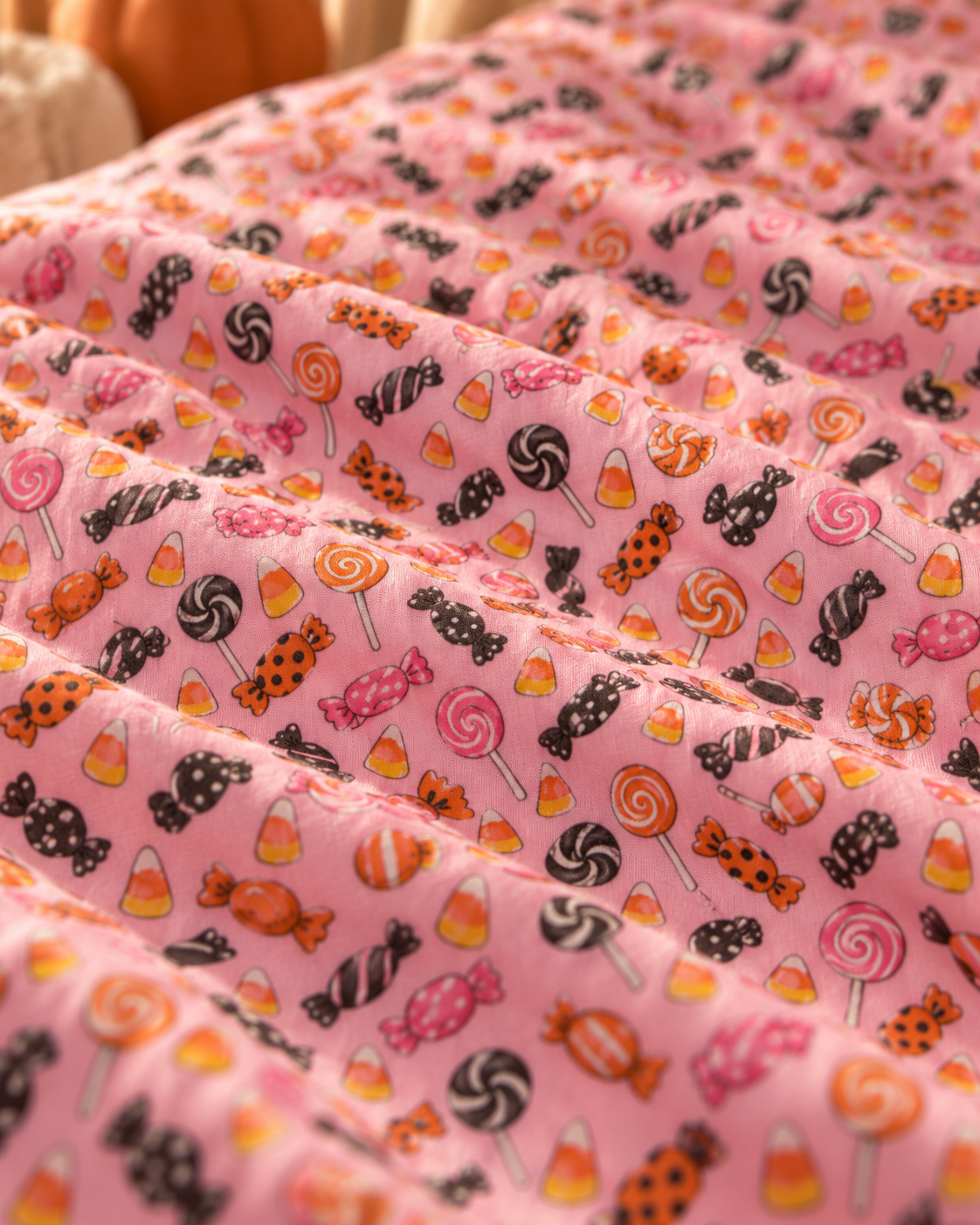 Close-up of the Halloween Candy Crib Sheet fabric showing wrapped candy, lollipops and candy corn on pink