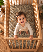 Toddler standing in a crib fitted with the Leopard Print Crib Sheet