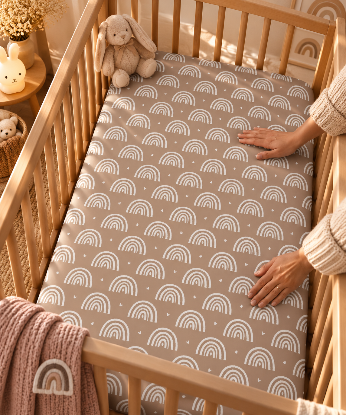 Hands smoothing the Mauve Boho Rainbow Crib Sheet over a crib mattress