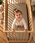 Toddler standing in a crib fitted with the Olive Heart Crib Sheet