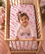 Toddler standing in a crib fitted with the Pink Bow Crib Sheet