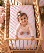 Toddler standing in a crib fitted with the Pink Candy Stripe Crib Sheet