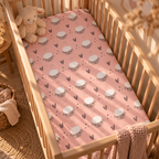 Pink Sheep Crib Sheet fitted in a wooden crib with a plush toy
