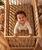 Toddler standing in a crib fitted with the Rust Boho Floral Crib Sheet