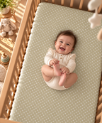Smiling baby lying on the Sage Polka Dot Crib Sheet