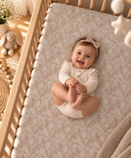Smiling baby lying on the Taupe Lace Floral Crib Sheet