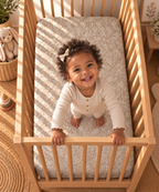 Toddler standing in a crib fitted with the Taupe Lace Floral Crib Sheet